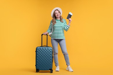 Happy young woman with passport, ticket and suitcase on yellow background