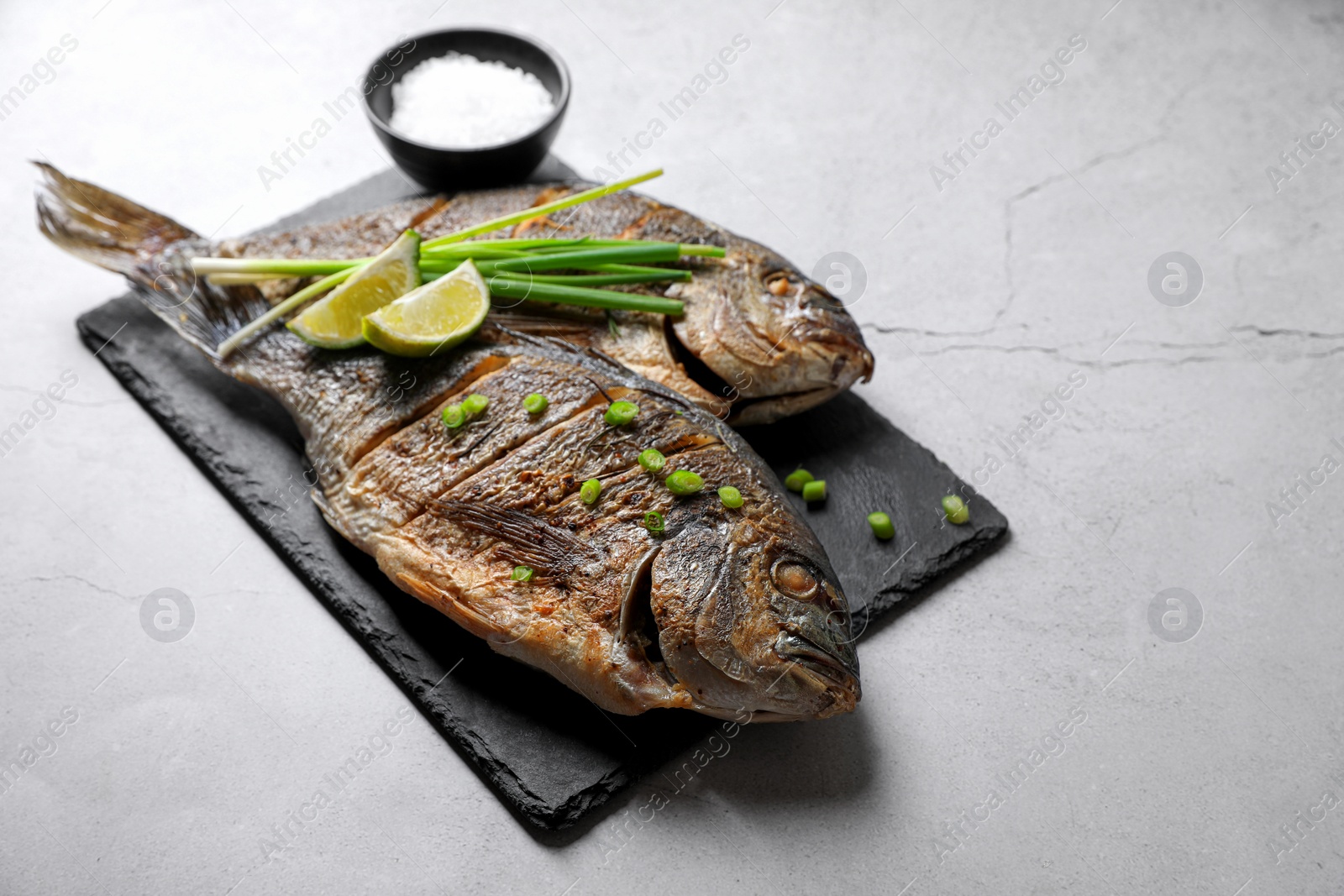 Photo of Seafood. Delicious baked fish served with green onion and lime on light textured table, space for text