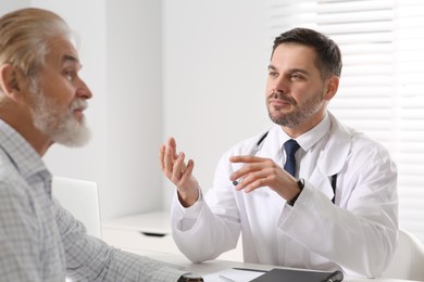 Photo of Doctor consulting senior patient at table in clinic