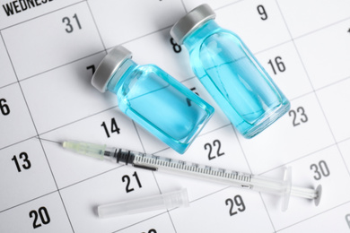 Photo of Vial and syringe on calendar, flat lay. Vaccination and immunization