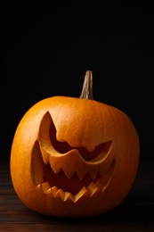Scary jack o'lantern made of pumpkin on wooden table in darkness. Halloween traditional decor