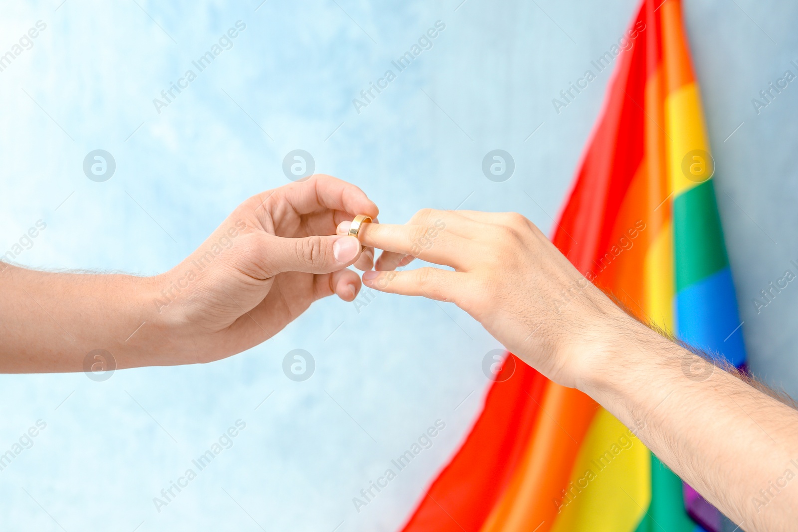 Photo of Young man putting wedding ring on his boyfriend's finger near rainbow flag. Gay marriage