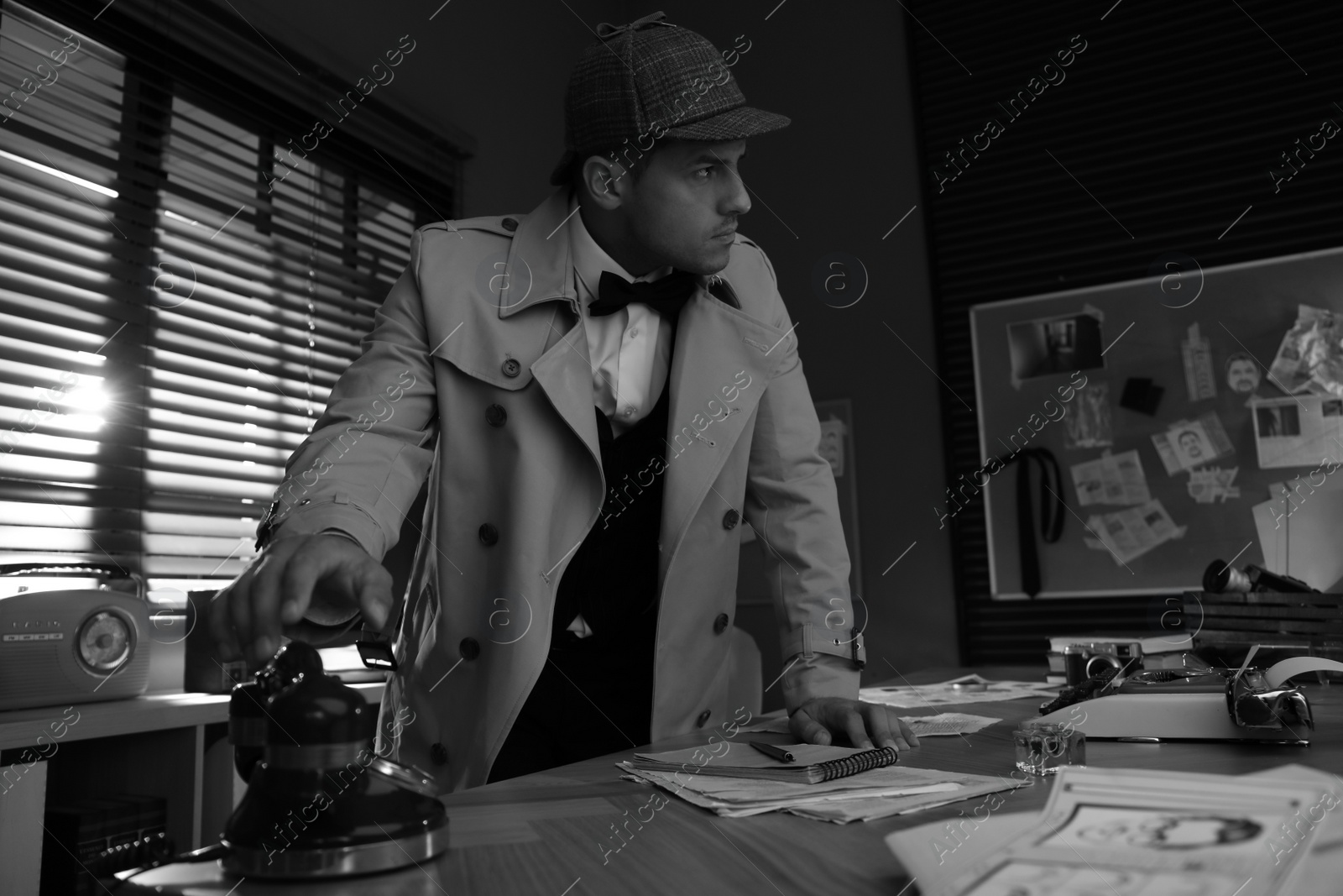 Photo of Old fashioned detective picking up phone in office. Black and white effect