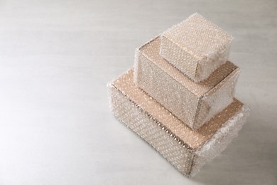 Photo of Cardboard boxes covered with bubble wrap on light grey table. Space for text