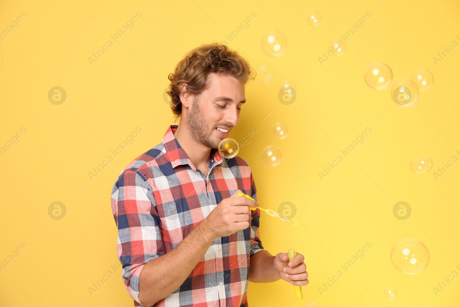 Photo of Young man blowing soap bubbles on color background