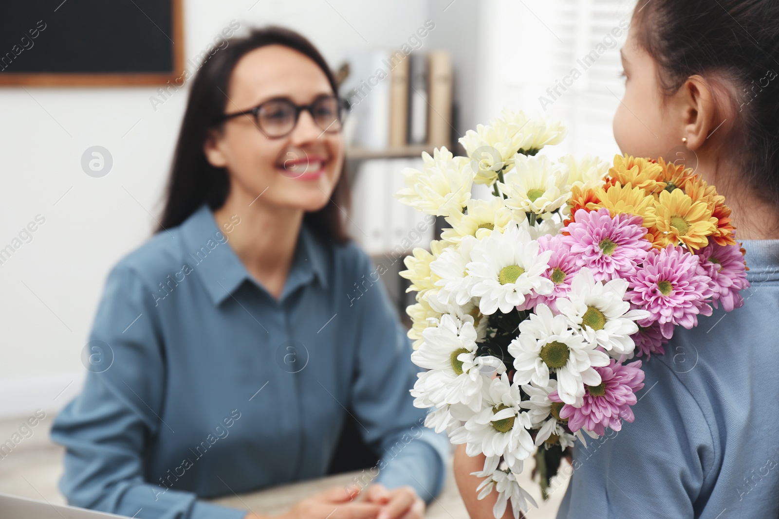 Photo of Schoolgirl with bouquet congratulating her pedagogue in classroom, closeup. Teacher's day