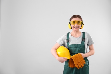 Photo of Female industrial worker in uniform on light background, space for text. Safety equipment