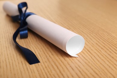 Photo of Graduation diploma tied with blue ribbon on wooden table, closeup