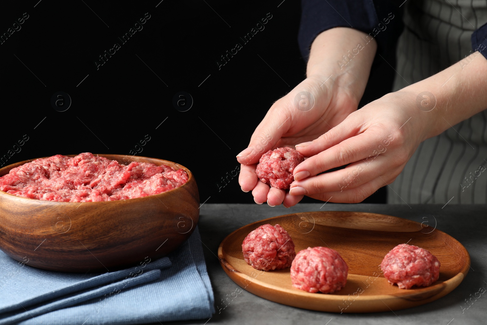 Photo of Woman making meatball from ground meat at grey table, closeup