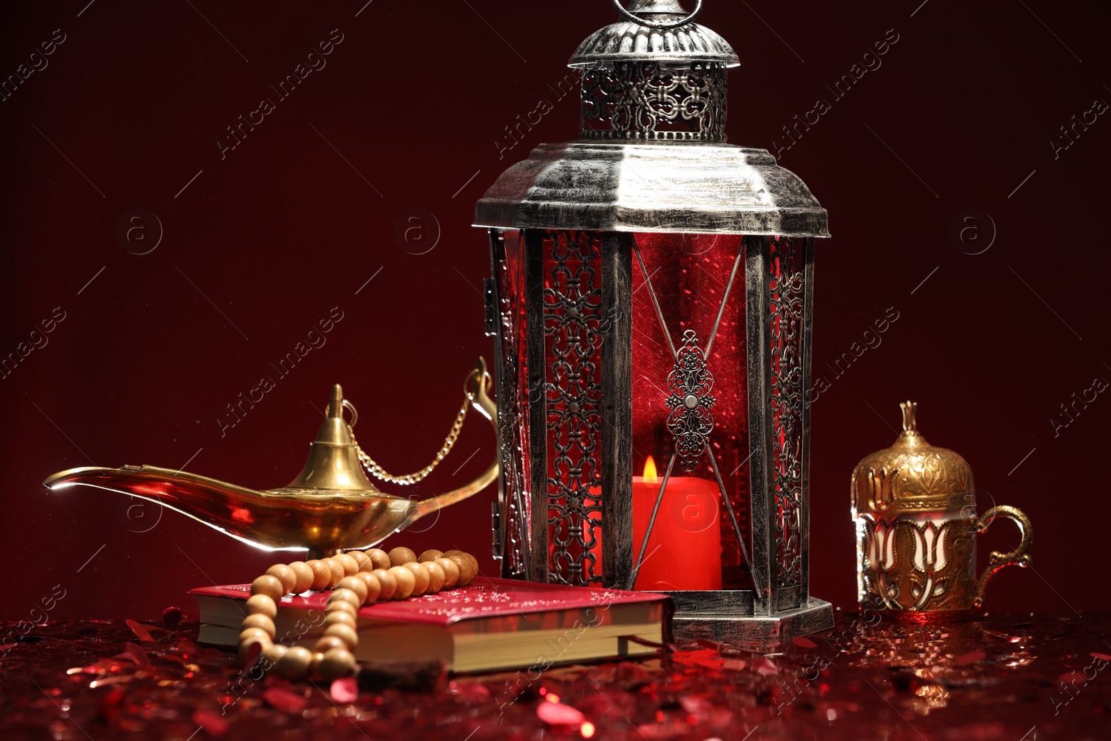 Photo of Arabic lantern, Quran, misbaha and Aladdin magic lamp on shiny red table