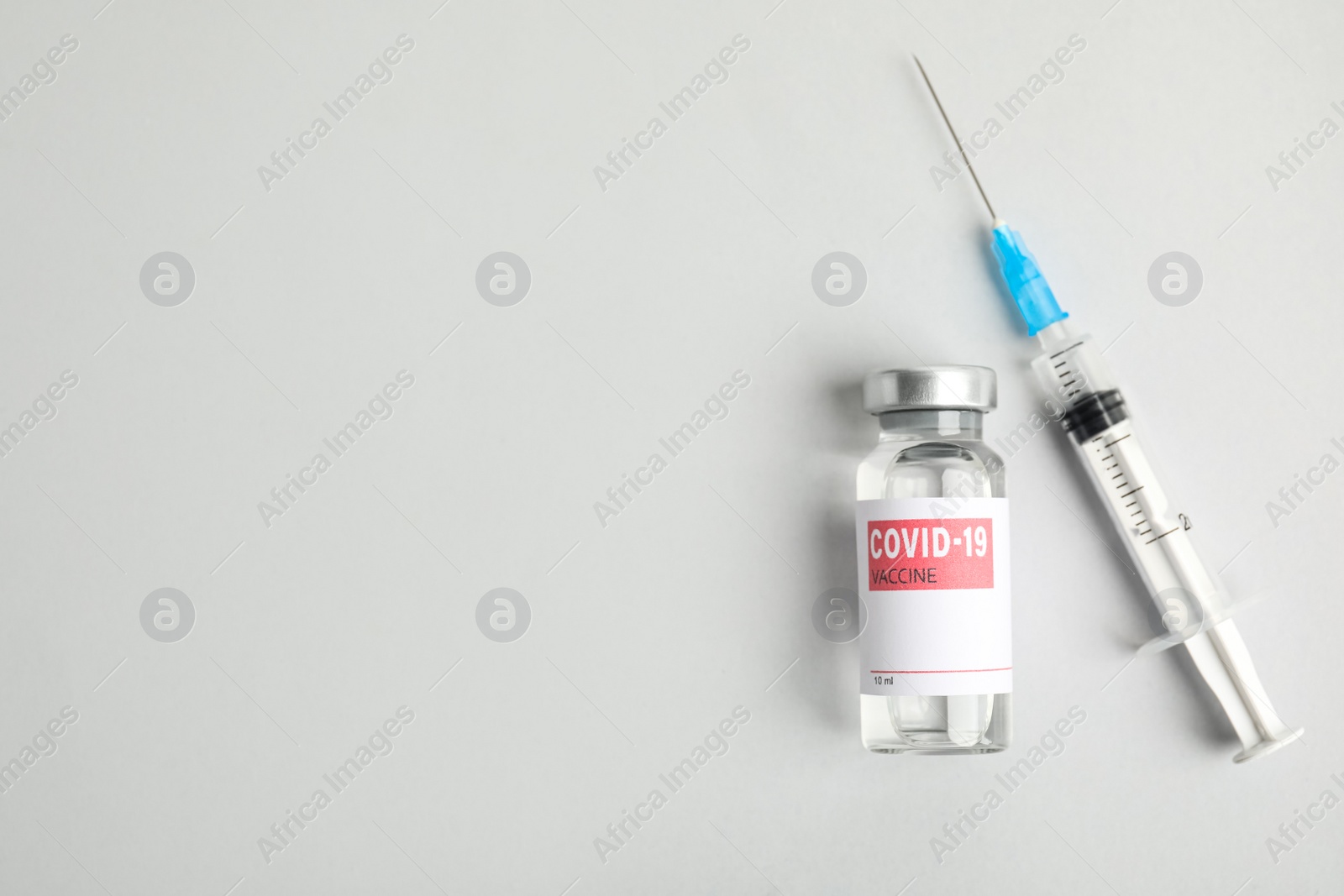 Photo of Vial with coronavirus vaccine and syringe on white background, flat lay. Space for text