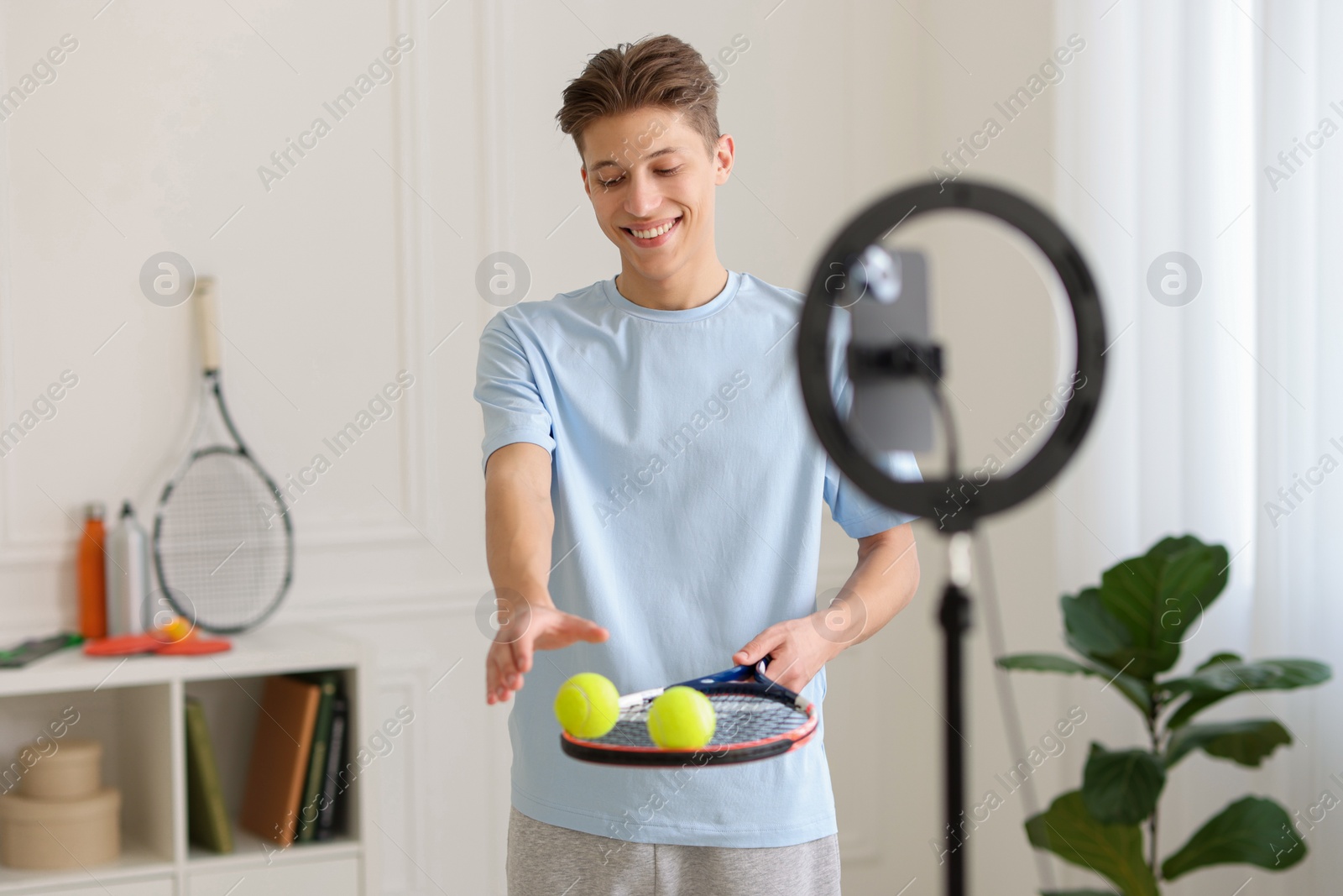 Photo of Smiling sports blogger with tennis racket and balls streaming online fitness lesson at home