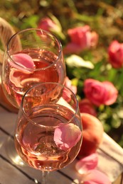 Glasses of delicious rose wine with petals on white picnic blanket outside, above view