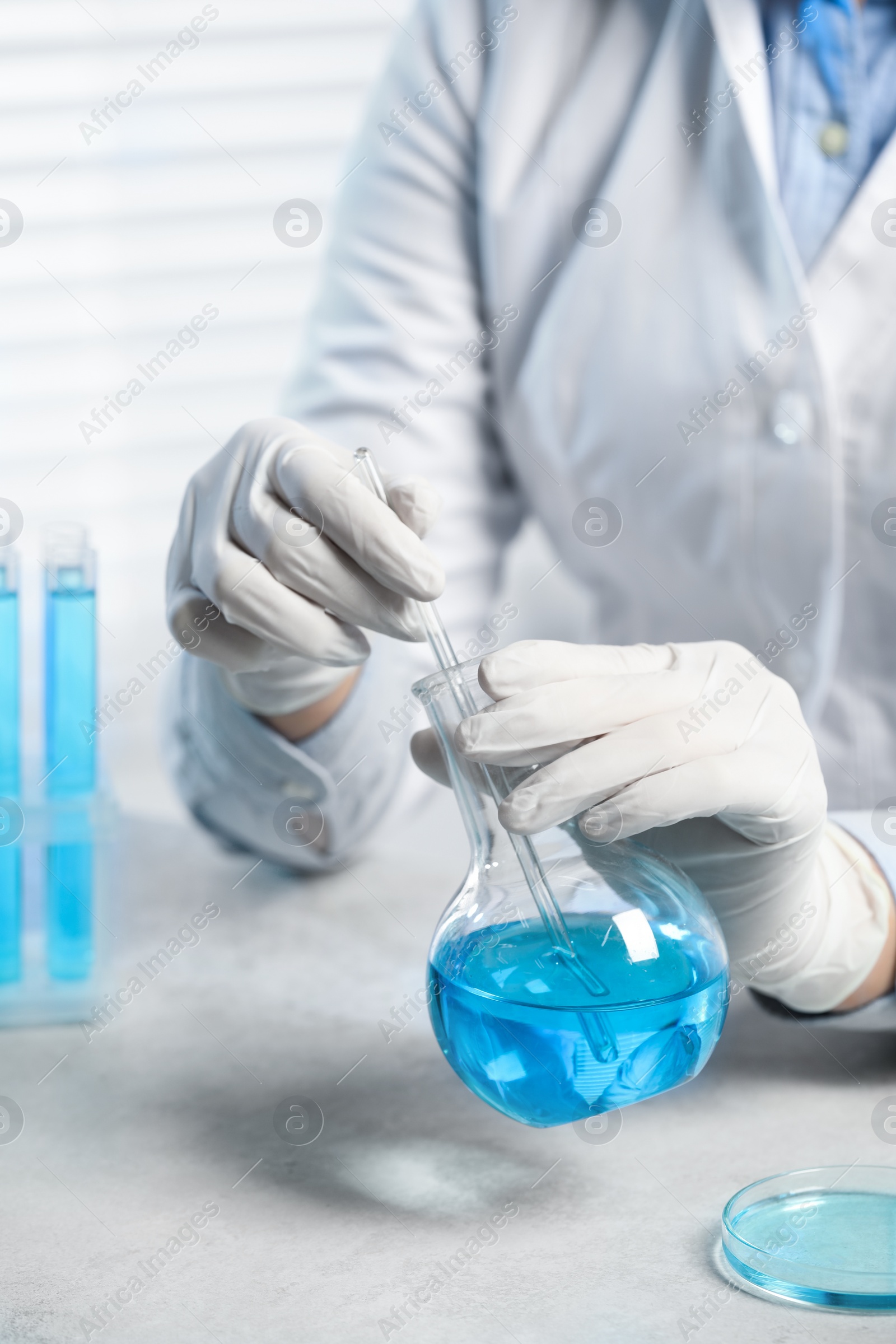 Photo of Scientist taking sample of light blue liquid at white table in laboratory, closeup