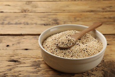 Photo of Raw quinoa seeds and spoon in bowl on wooden table, closeup. Space for text