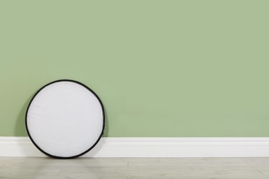 Studio reflector near pale green wall in room, space for text. Professional photographer's equipment