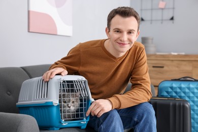 Travel with pet. Man near carrier with cute cat on sofa at home