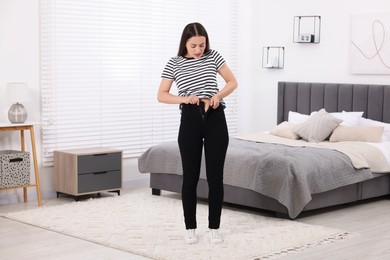 Woman trying to put on tight jeans in bedroom
