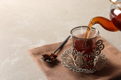 Photo of Pouring traditional Turkish tea from pot into glass on table. Space for text