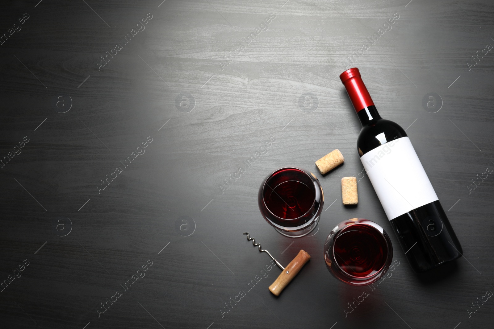Photo of Glasses and bottle with red wine on dark background, flat lay. Space for text