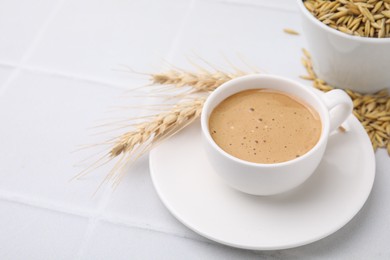 Cup of barley coffee, grains and spikes on white table, closeup. Space for text