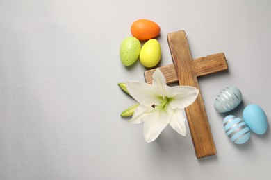 Wooden cross, painted Easter eggs and lily flowers on grey background, flat lay. Space for text