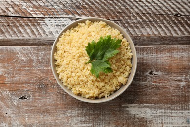 Photo of Delicious bulgur and parsley in bowl on wooden table, top view