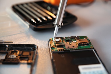 Photo of Repairing broken mobile phone with soldering iron on table, closeup