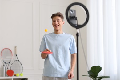 Smiling sports blogger with table tennis racket and ball streaming online fitness lesson at home