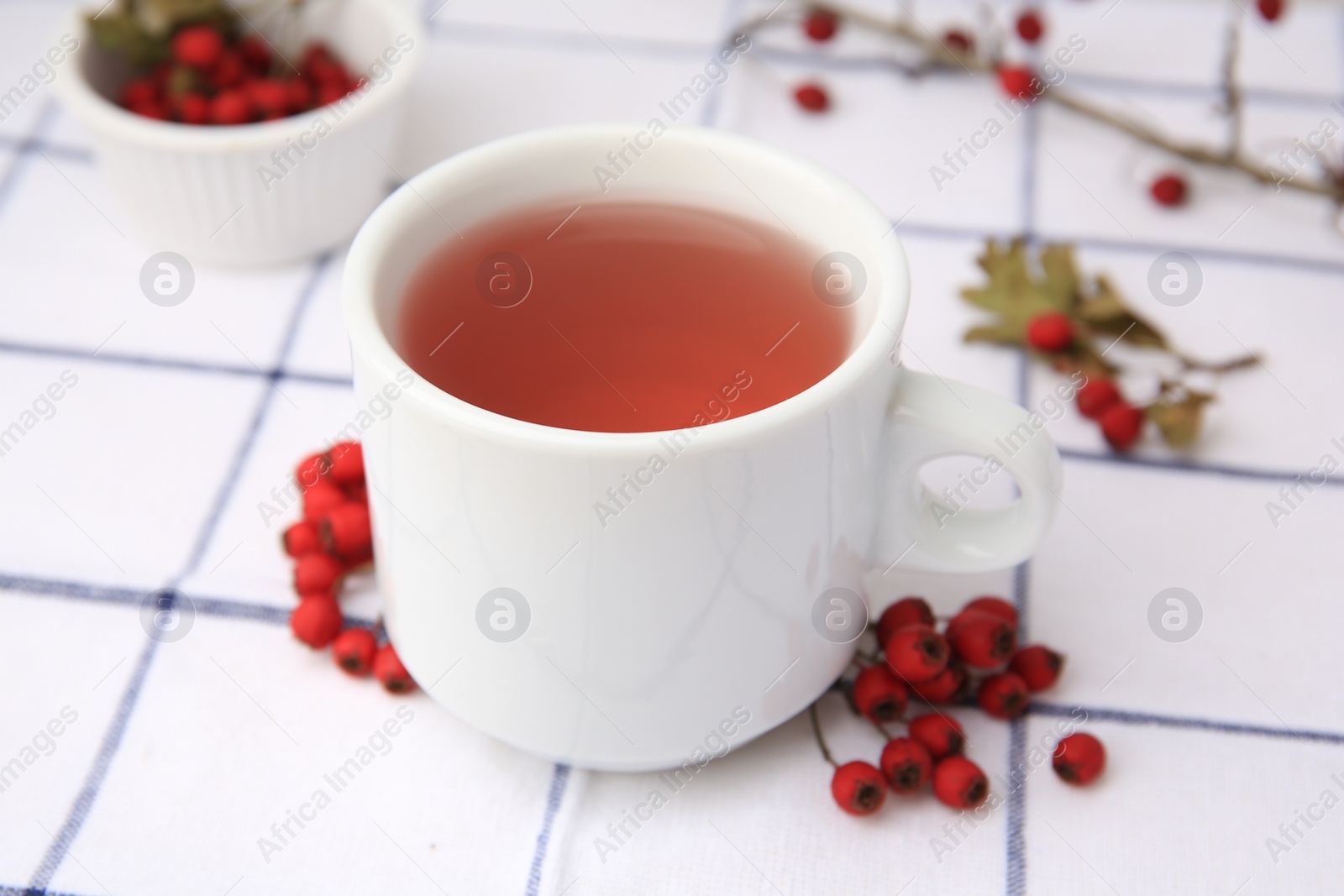 Photo of Cup with hawthorn tea and berries on table, closeup
