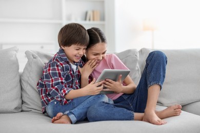 Photo of Happy brother and sister with tablet on sofa at home