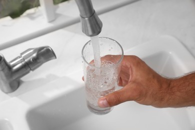 Photo of Man filling glass with water from tap at home, closeup