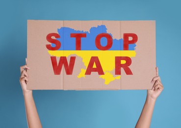 Image of Woman holding poster with words Stop War and map of Ukraine in national colors on light blue background, closeup