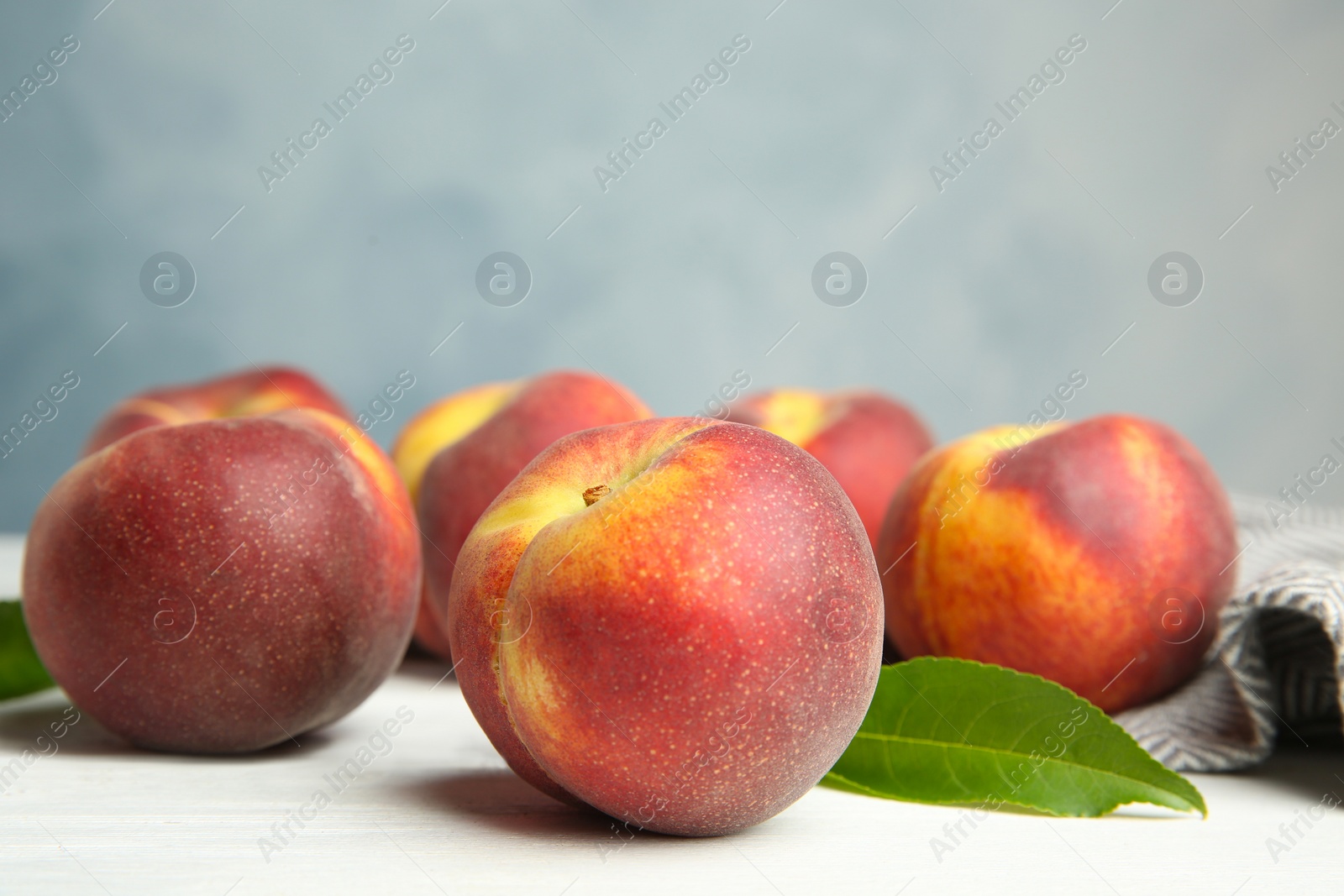 Photo of Fresh juicy peaches, leaves and fabric on white wooden table