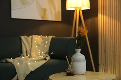 Photo of Vase with beautiful flower and air freshener on wooden coffee table near sofa in room