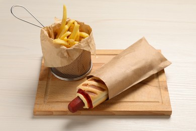 Photo of Delicious french hot dog and fries on white wooden table