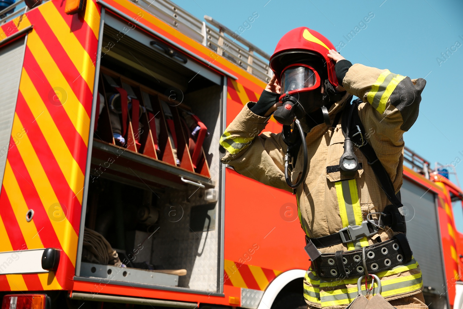 Photo of Firefighter in uniform wearing helmet and mask near fire truck outdoors, low angle view