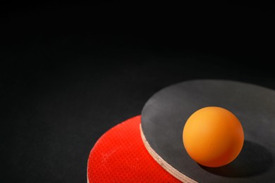 Photo of Ping pong ball and rackets on black background, closeup. Space for text