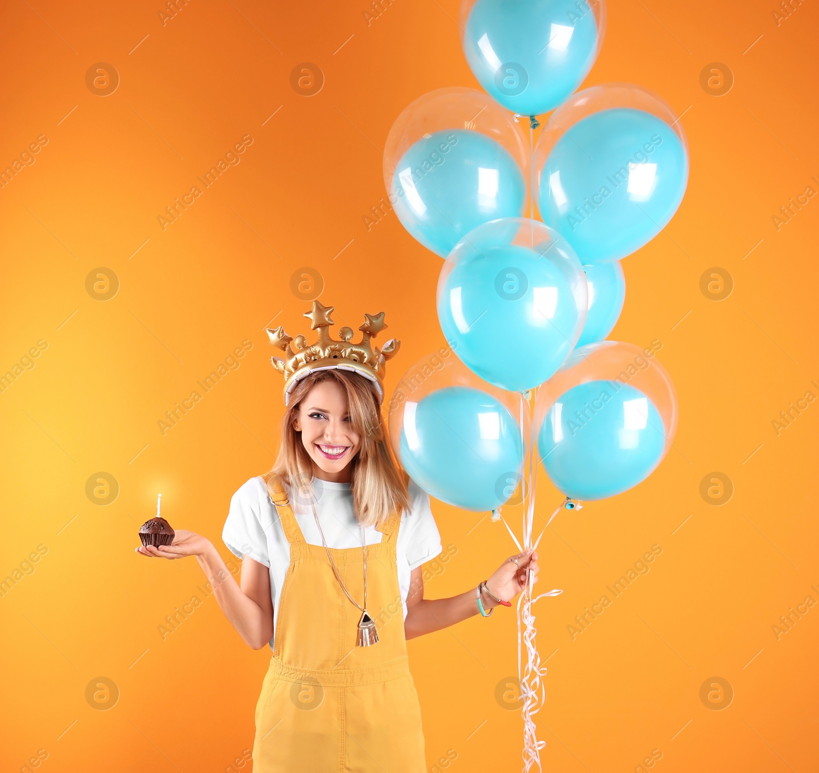 Photo of Young woman with birthday muffin and air balloons on color background