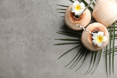 Photo of Fresh coconuts with drinking straws and flowers on grey table, flat lay. Space for text