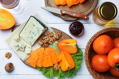 Delicious persimmon, blue cheese and nuts served on white wooden table, flat lay