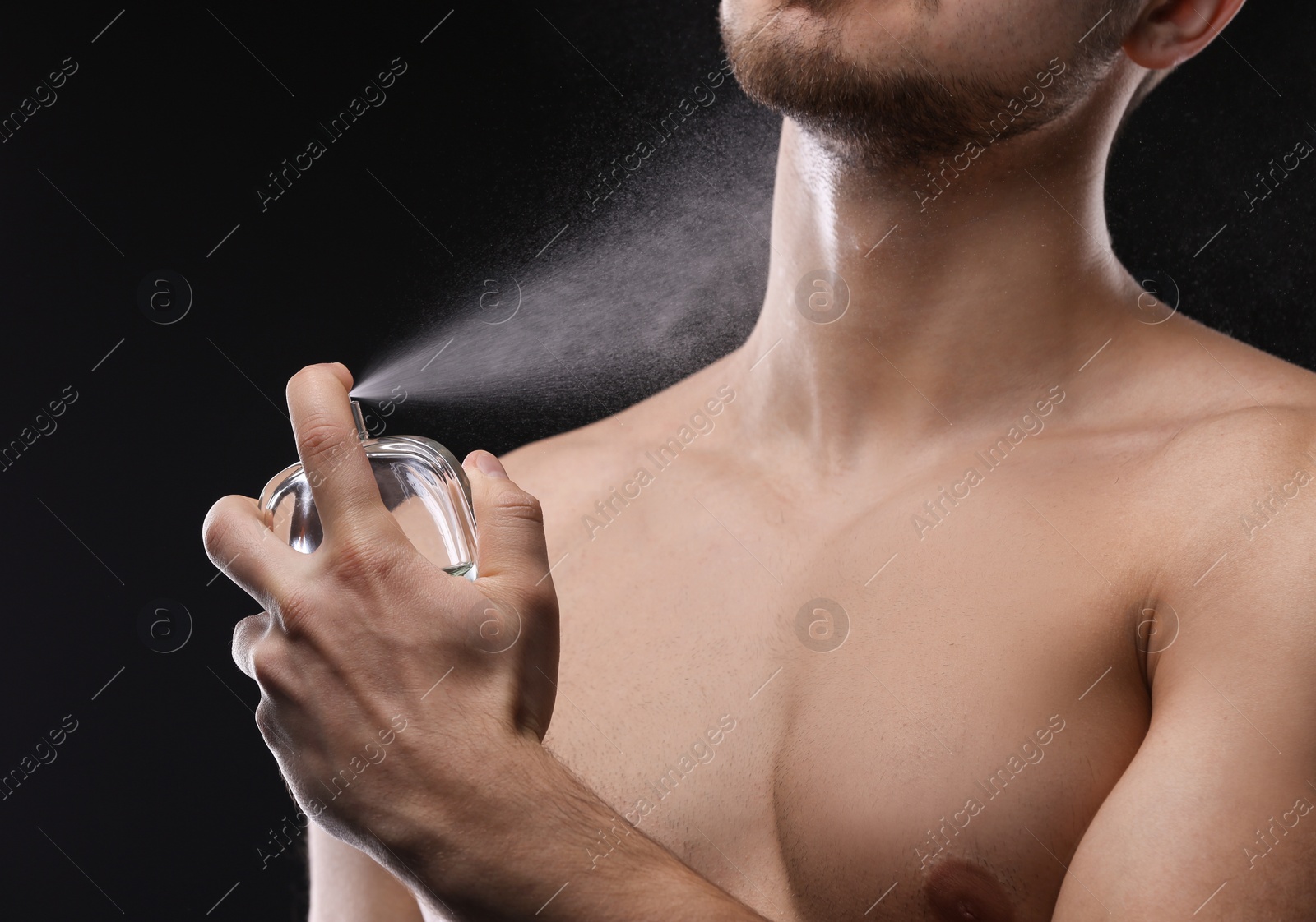 Photo of Handsome man using perfume on black background, closeup