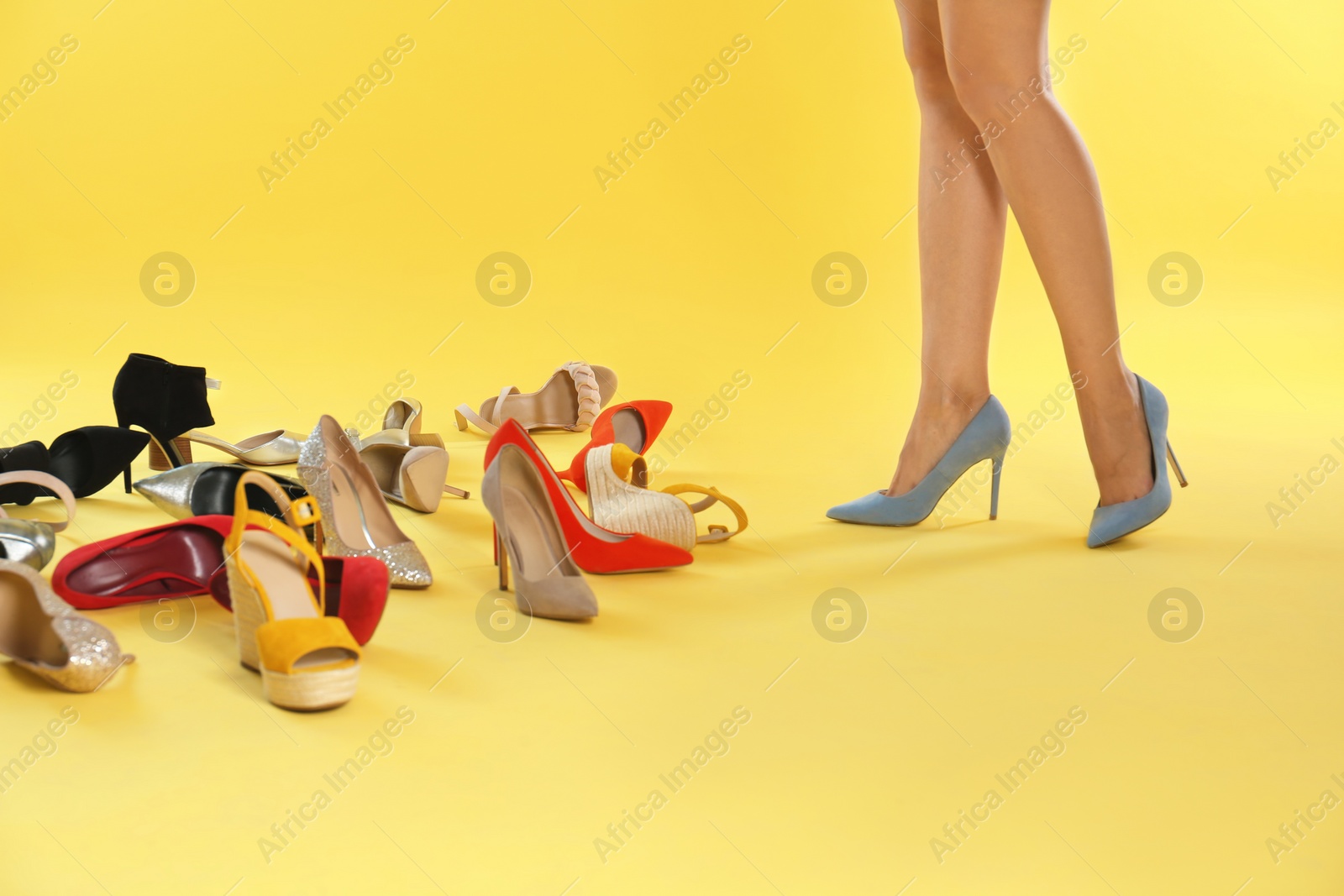 Photo of Woman trying on different high heel shoes on yellow background, closeup