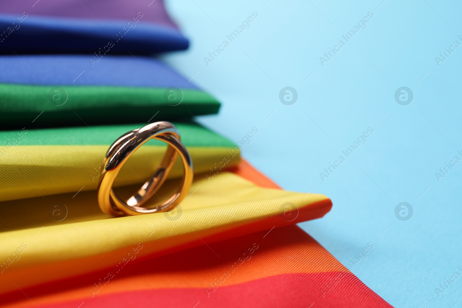 Photo of Rainbow LGBT flag and wedding rings on light blue background, closeup. Space for text