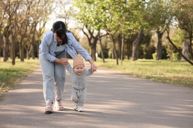 Mother supporting her baby while he learning to walk outdoors. Space for text