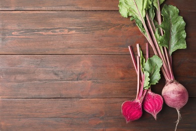 Cut and whole raw beets on wooden table, flat lay. Space for text