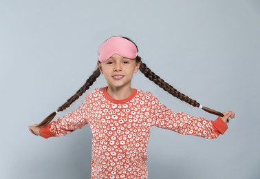 Photo of Cute girl in pajamas with pink sleep mask on light grey background