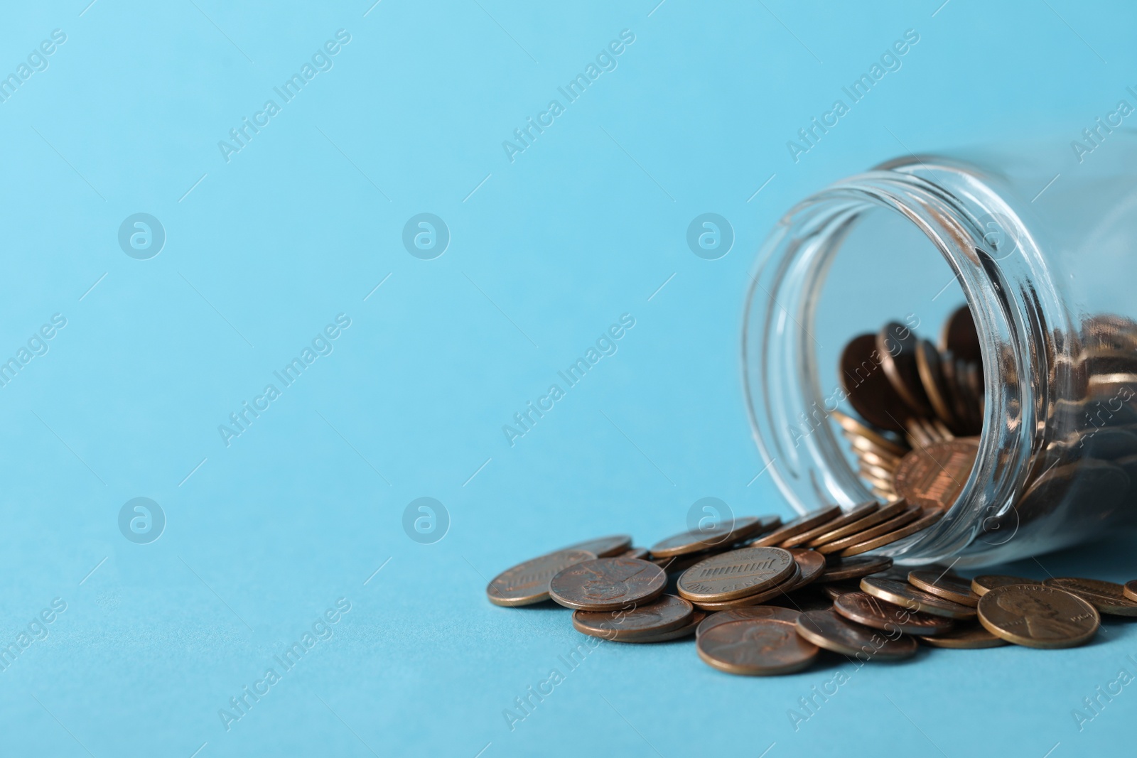 Photo of Glass jar with coins on light blue background, closeup. Space for text