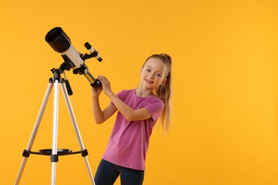 Photo of Happy little girl with telescope on orange background, space for text