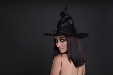 Photo of Mysterious witch wearing hat on black background, space for text